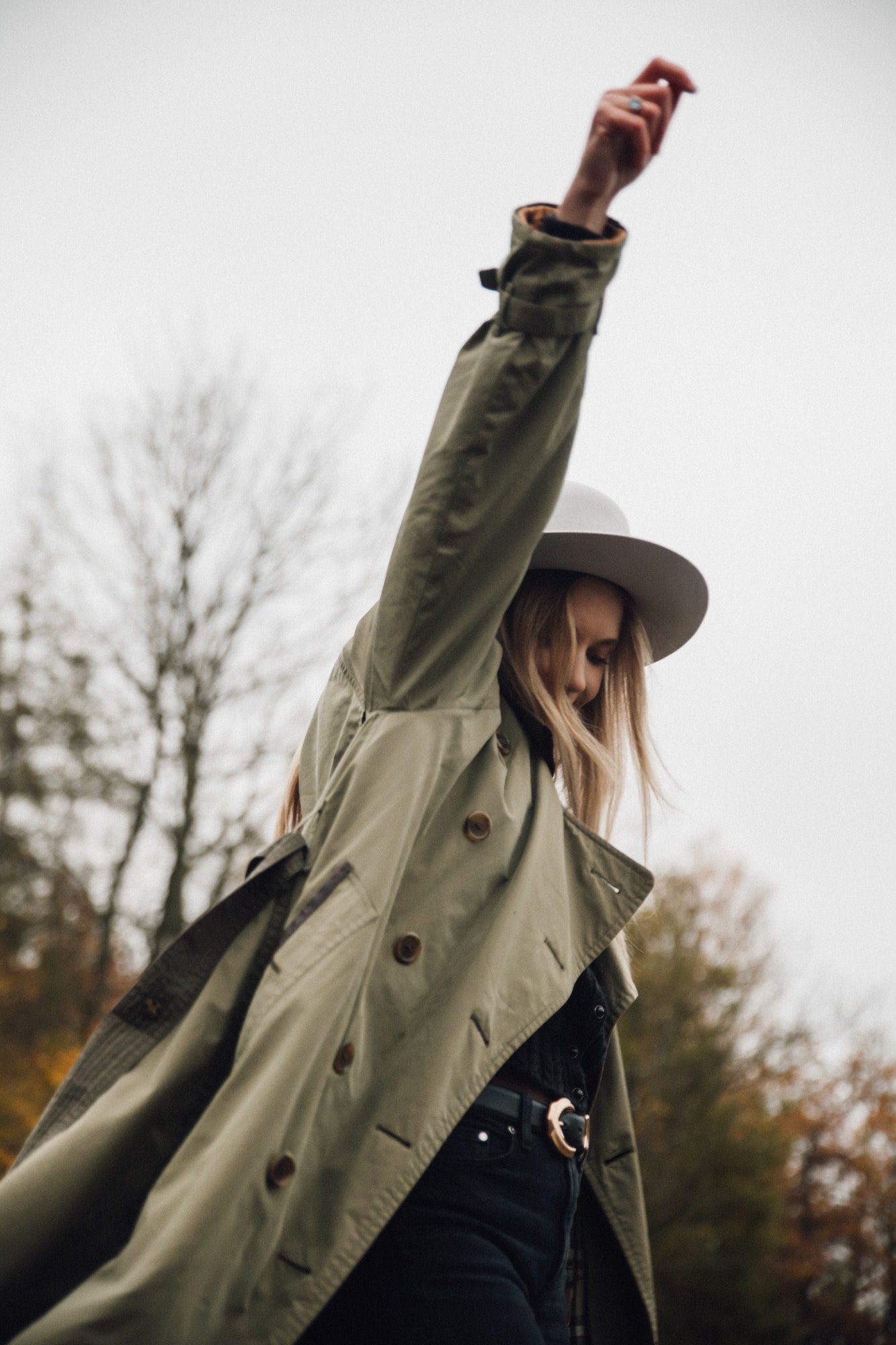 Portrait from below of a young blonde woman with hands in the air in warm clothes in nature.