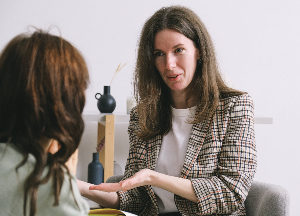 Therapist in plaid blazer attentively listening and speaking to client during a therapy session.